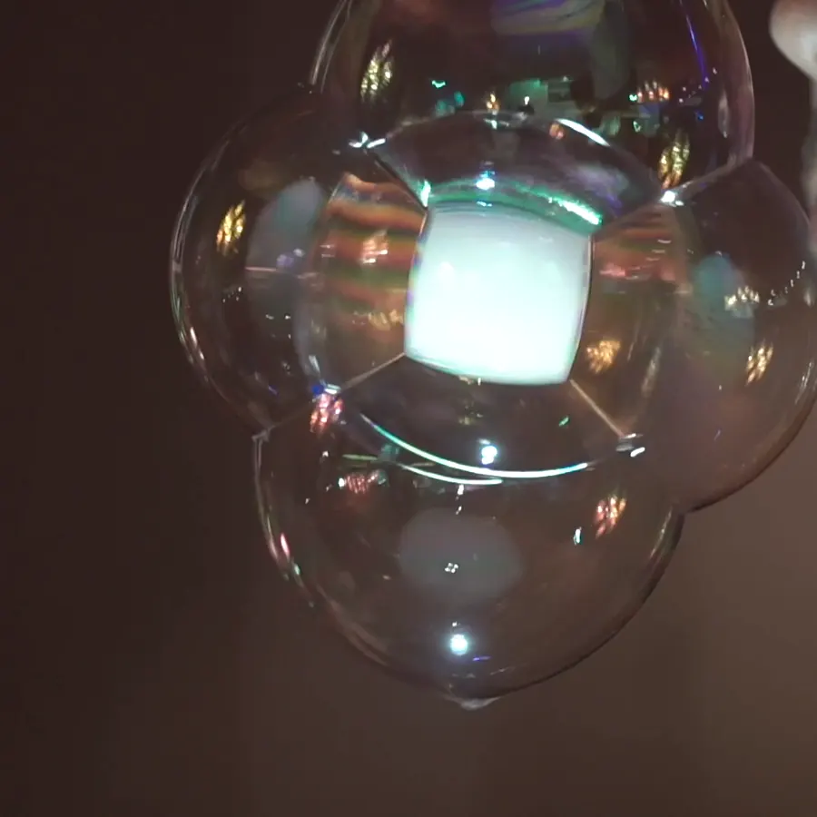 Grappe de bulles de savon éclairée de l'intérieur, suspendue devant un visage